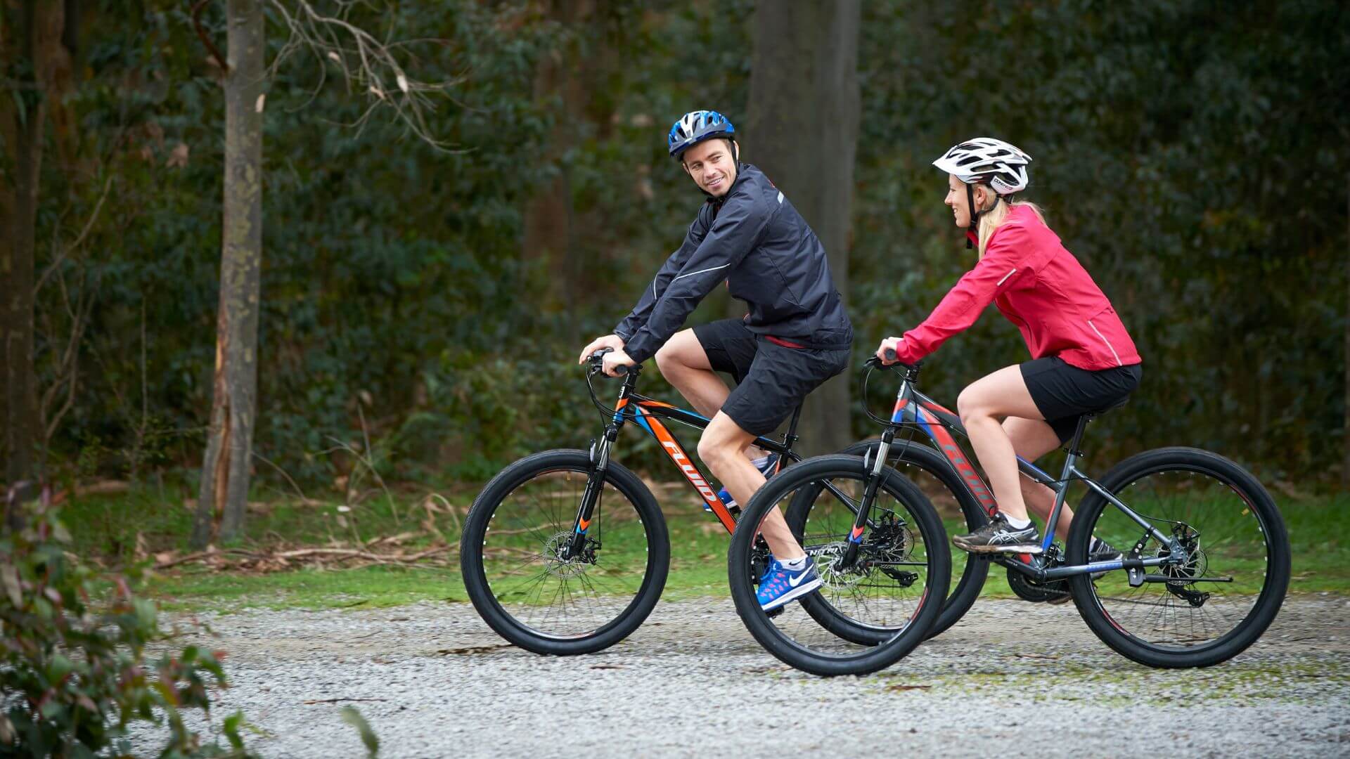 Man & Woman Riding Fluid Mountain Bikes On A Trail