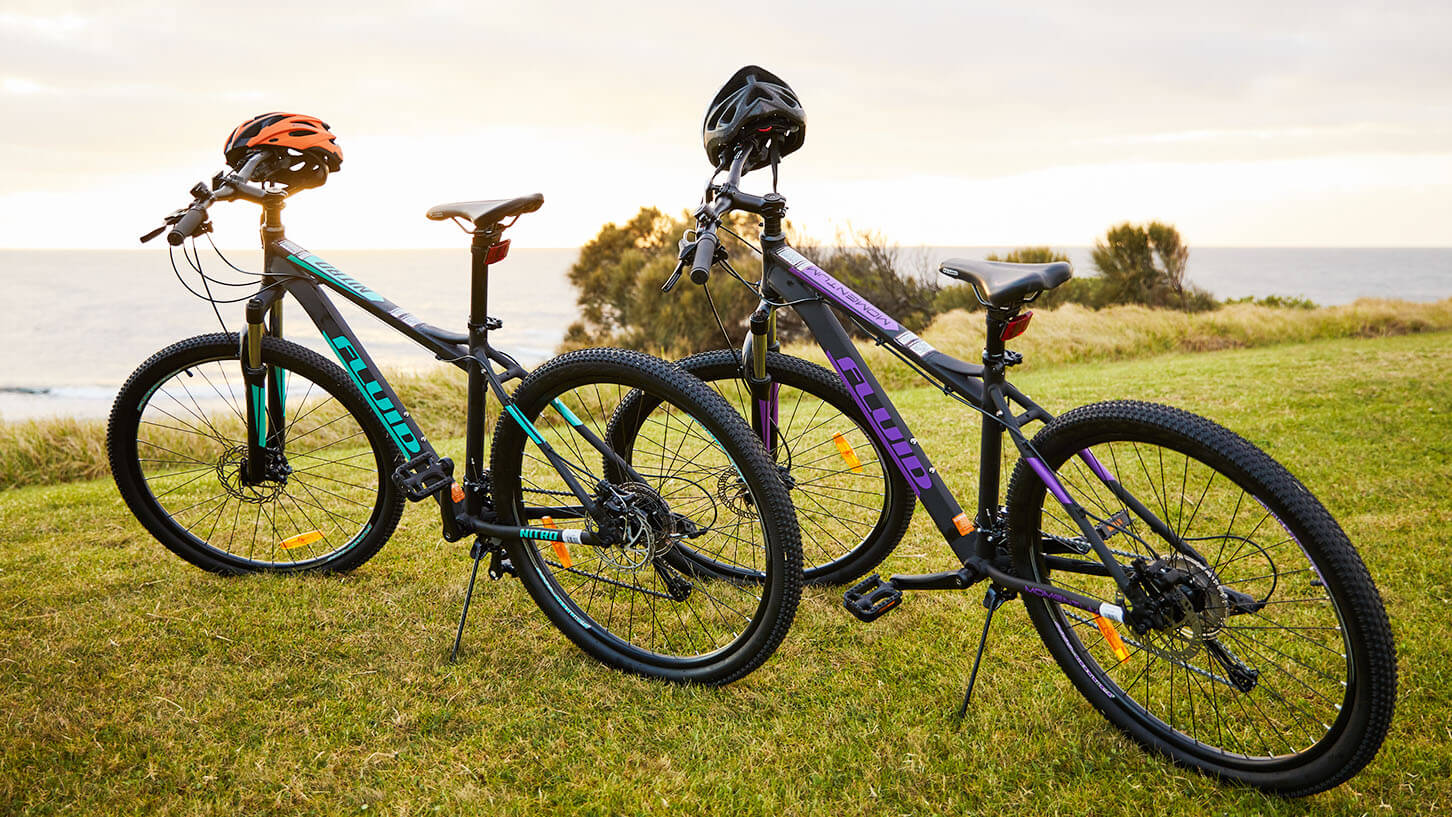 Fluid Mountain Bikes & Helmets Parked On Grass By The Beach