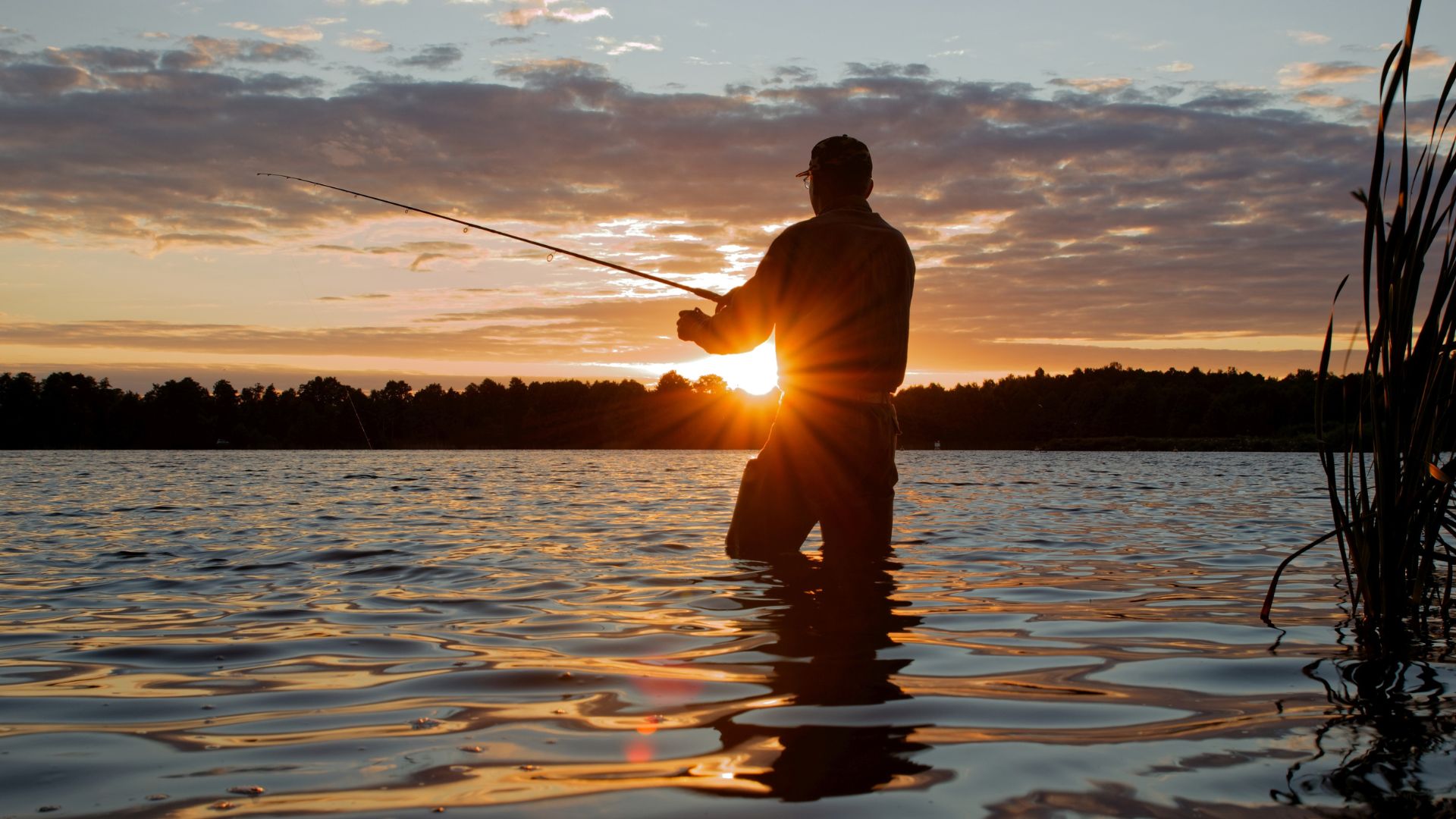 Silhouette of a man knee-deep in water fishing at sun down