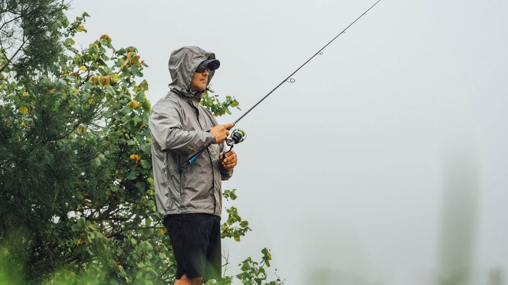 Man Wearing Sunglasses, Cap And Hooded Waterproof Jacket Fishing