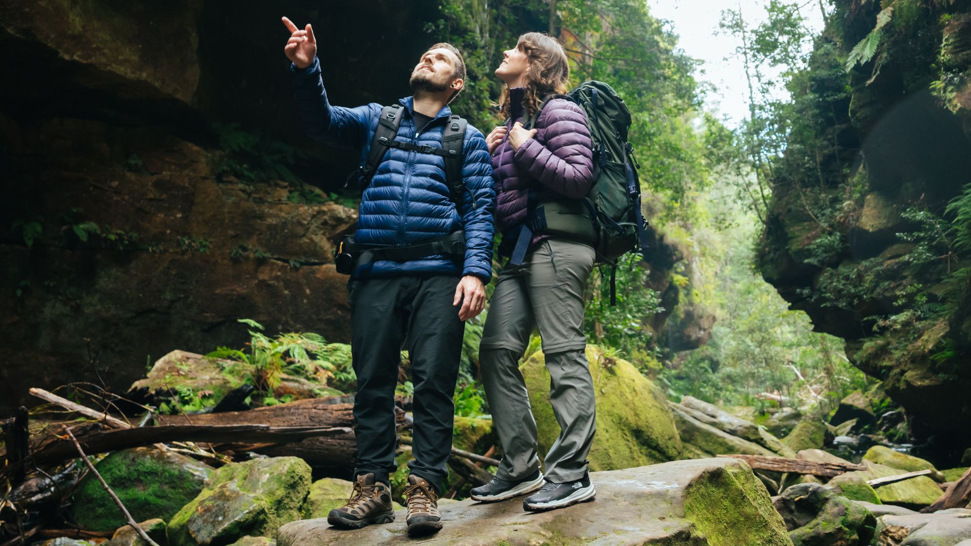 Two hikers wearing puffer jackets, day packs, hiking pants and mid hiking boots